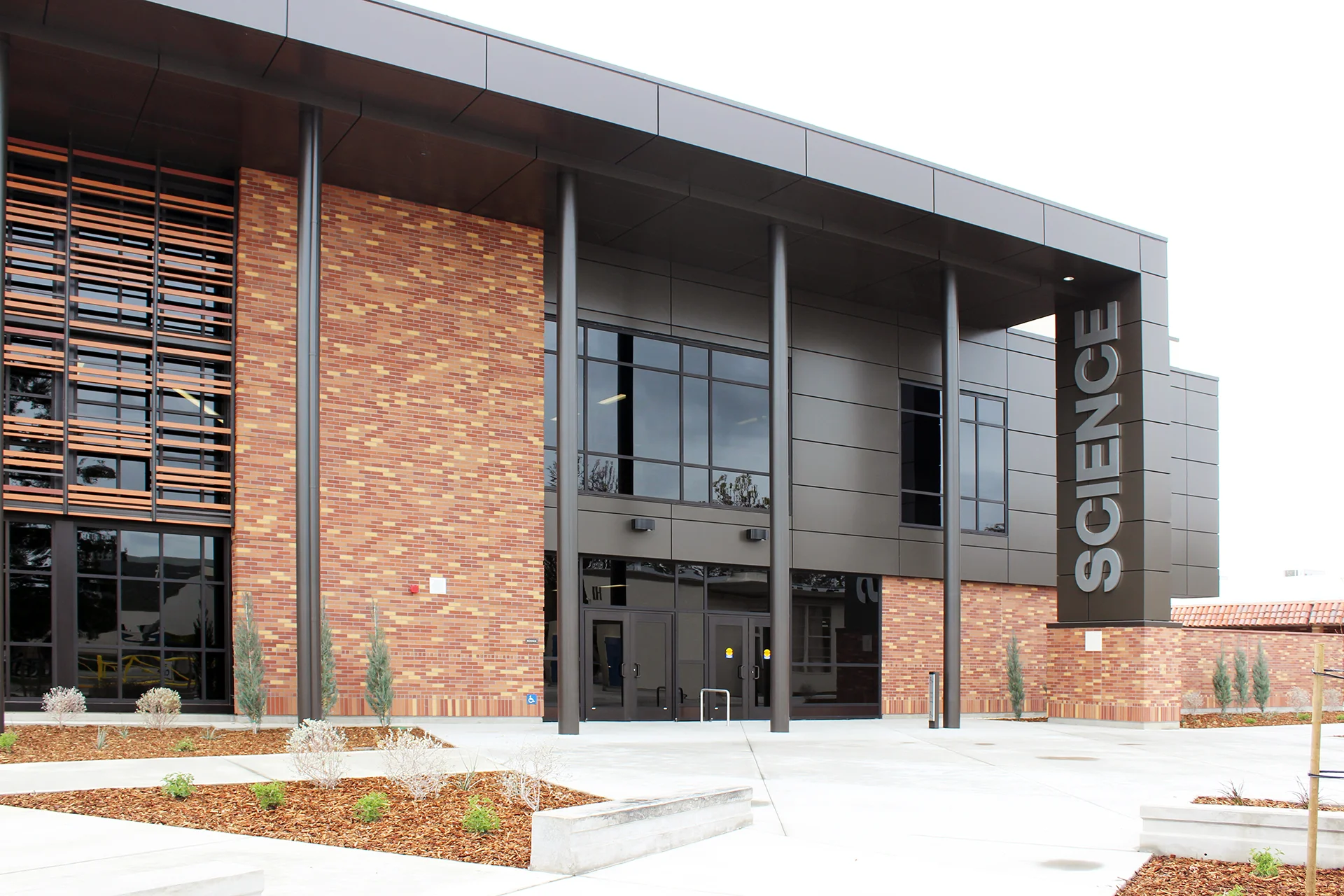 Main entrance of the Turlock High School Science Building featuring contemporary brick and metal architecture, floor-to-ceiling windows, covered entry, and dedicated STEM education facilities.