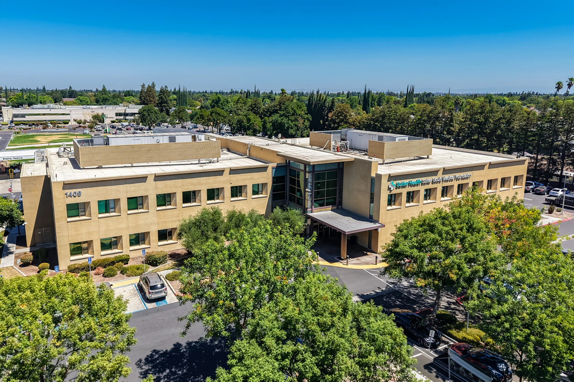 Main entrance of the Sutter Gould Briggsmore Specialty Center featuring a glass atrium, covered patient drop-off, illuminated healthcare facility, and contemporary medical office architecture at dusk.