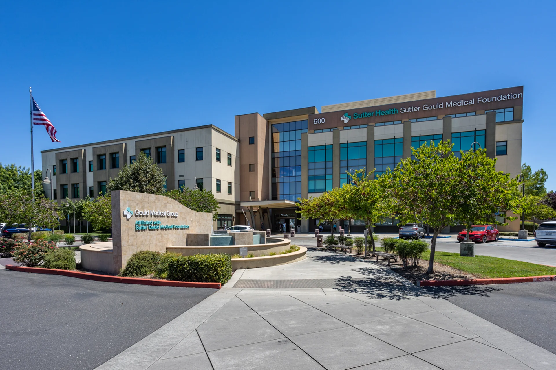 Front entrance of the Sutter Gould Coffee Road Medical Office Building featuring the Gould Medical Group monument sign, landscaped fountain, patient drop-off, and modern healthcare facility in Modesto, California.